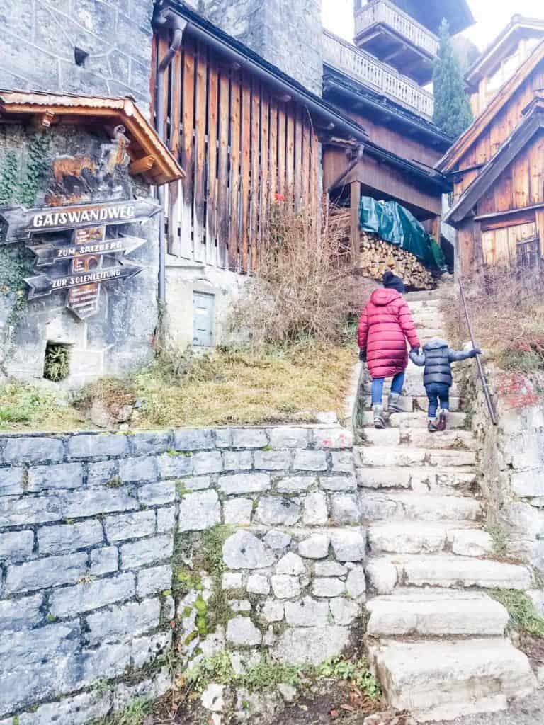 Mom and son walking up stones stairs toward wooden house in Hallstatt Austria in the winter