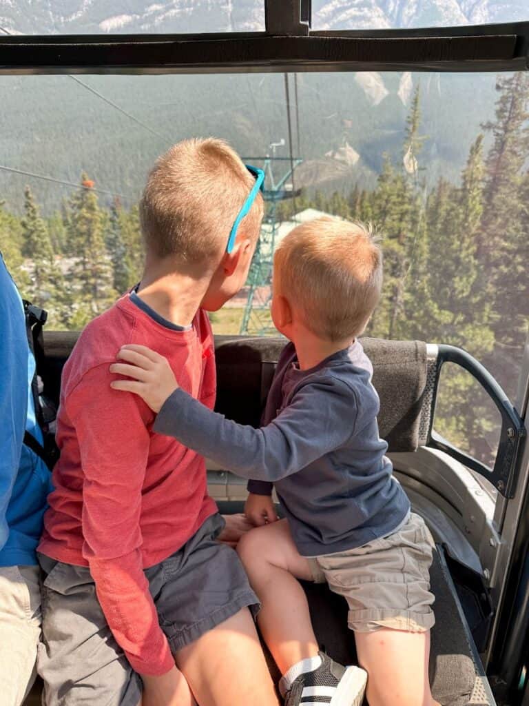 Brothers looking out window of Banff Gondola during Banff itinerary with kids