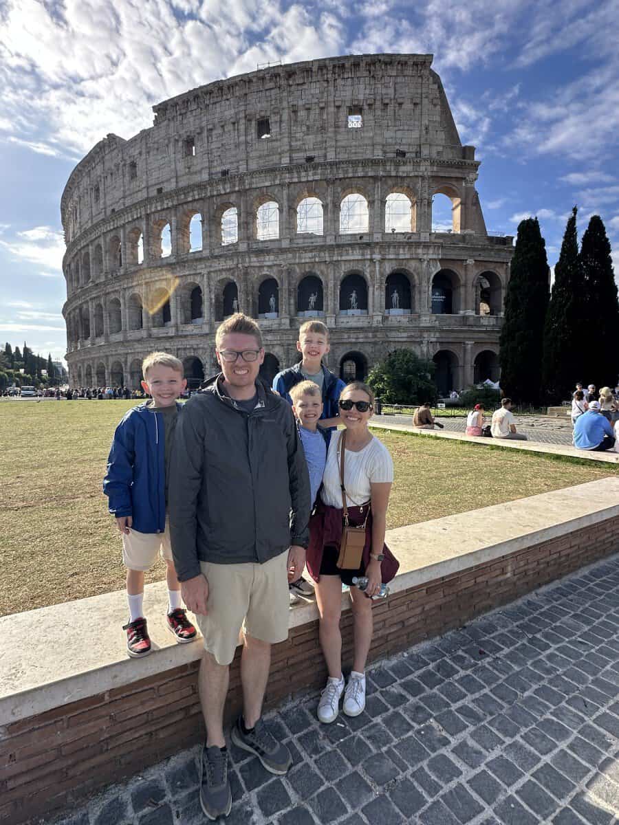 Family posing in front of the Colosseum in Rome on a sunny day.